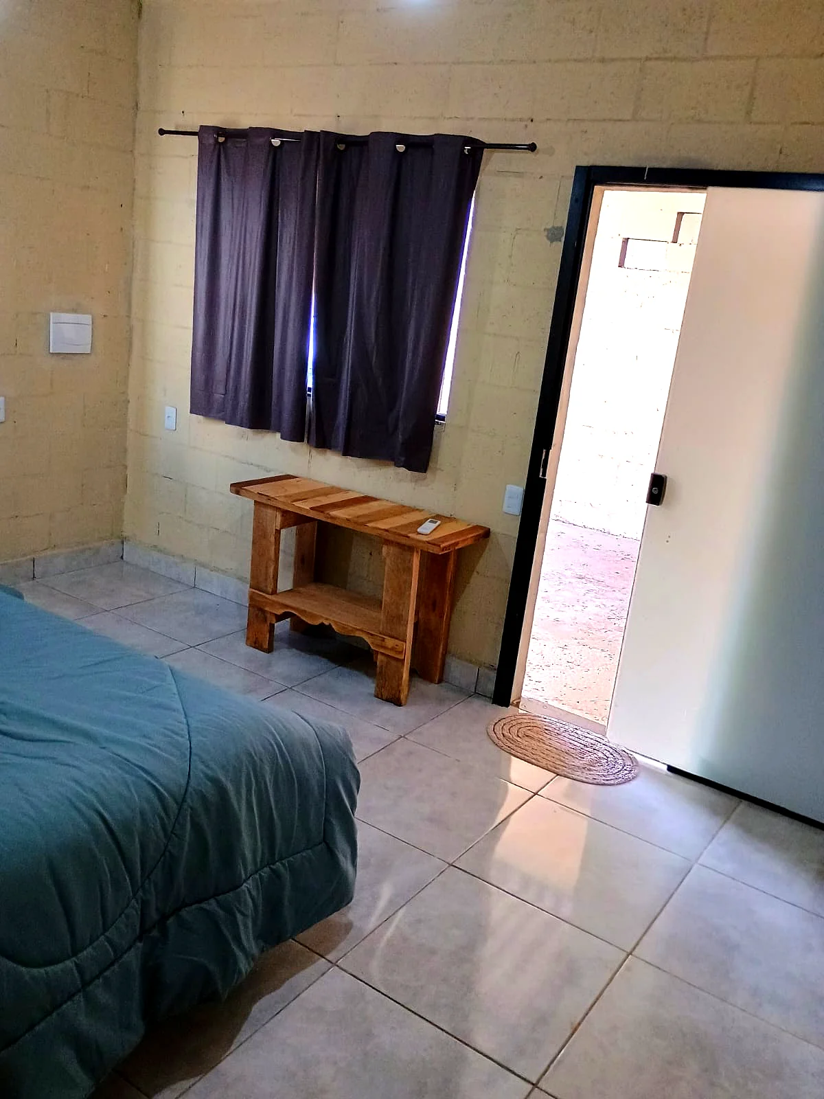 Interior do quarto com banco em madeira maciça e cama de casal — Pousada Vale do Jamacá